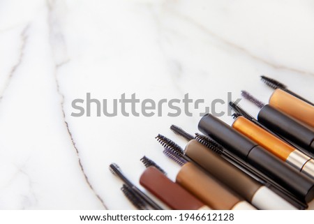Flat lay of composition of mascara brushes, mascara for eyelash and eyebrow on white marble background. Eyebrow grooming concept. Cosmetic and makeup tool with copy space. Beauty treatment.