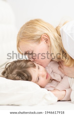 Mom kissing a girl with down syndrome in the bedroom on the bed while going to bed. Ordinary childcare in a family for children with disabilities 
