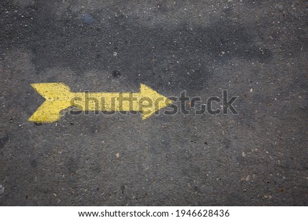 Yellow arrow painted on concrete sidewalk pointing right