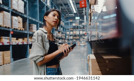 Attractive young Asia businesswoman manager looking for goods using digital tablet checking inventory levels standing in retail shopping center. Distribution, Logistics, Packages ready for shipment. Royalty-Free Stock Photo #1946631142