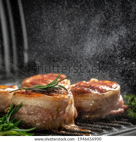 Medallions steaks from the beef tenderloin covered bacon on grill with smoke dark background.