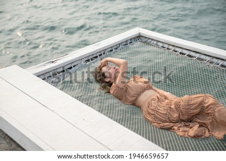 Woman lying on a pier with sea background, sit on the net by the sea.