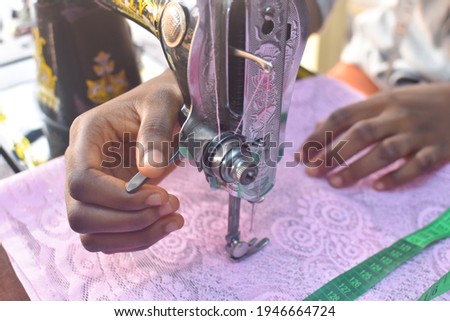 African tailor or fashion designer sewing a pink cloth with measuring tape beside the sewing machine 