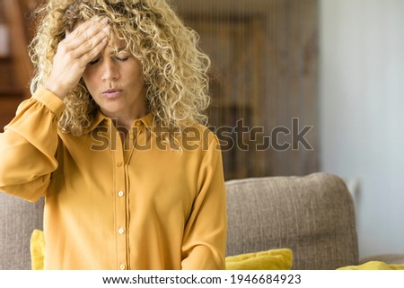 Young adult woman at home suffers from headache sitting on the sofa while work on laptop computer - tired and stressed people job smart working concept lifestyle - healthy disease Royalty-Free Stock Photo #1946684923