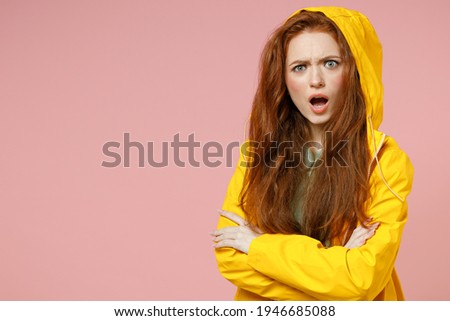 Redhead young indignant confused woman in yellow waterproof raincoat outerwear hood hold hands crossed folded isolated on pastel pink background studio Outdoors lifestyle weather fall season concept