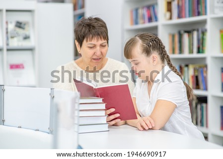Teacher and girl with syndrome down read a book at library. Education for disabled children concept Royalty-Free Stock Photo #1946690917