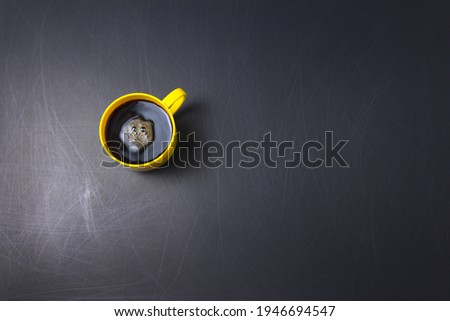 Yellow cup, mug of black coffee with clockwise stir flat lay on scrathed rough black background. Copy space for your text, image or message. Minimal, horizontal image style.
