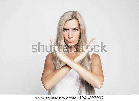 Elderly woman with long gray hair wearing casual style rejection expression crossing arms doing negative sign, angry face over grey background.