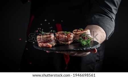 Cooking beef steak by chef hands. Medallions steaks from the beef tenderloin covered bacon on dark background. banner, menu recipe place for text.