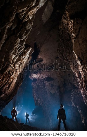 Speleologists wondering and admiring a gigantic cave chamber. Caving is a science and extreme sport dedicated to discover new underground unexplored passages Royalty-Free Stock Photo #1946718820