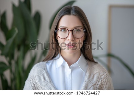 Waist up picture of long-haired woman in eyeglasses looking confident