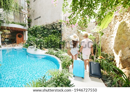 Young couple with suitcases walking to room of luxurious spa resort, view from the back Royalty-Free Stock Photo #1946727550