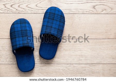 Blue slippers on parquet floor. Picture taken at home representing a pair of tartan fabric slippers abandoned on the floor.