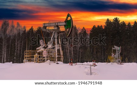 Oil pump jack winter working. At the orange sunset dawn of the sky with clouds. Oil rig energy industrial machine for petroleum in the sunset background for design. Nodding donkey
