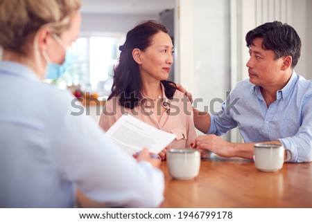 Worried Mature Asian Couple At Home Meeting With Female Healthcare Worker In Mask During Pandemic