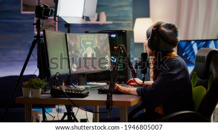 Woman streamer checking sound using professional mixer for streaming video games in gaming home studio. Pro gamer playing first person shooter video games talking with team mates on open chat Royalty-Free Stock Photo #1946805007