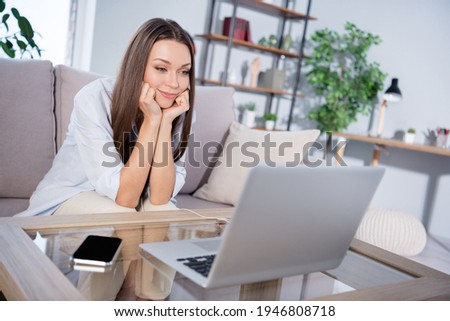 Photo of happy positive smiling beautiful woman sit sofa watching video in laptop computer enjoying beak pause at home