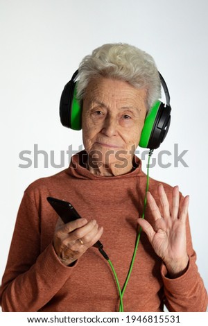 Older woman enjoying music from smart phone. Wearing green headphones, Waving with her hand. Technology concept. white background.