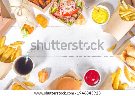 Delivery fastfood ordering food online concept. Large set of assorted take out foods pizza, french fries, fried chicken nuggets, burgers, salads, chicken wings, various sides, white table background  Royalty-Free Stock Photo #1946843923