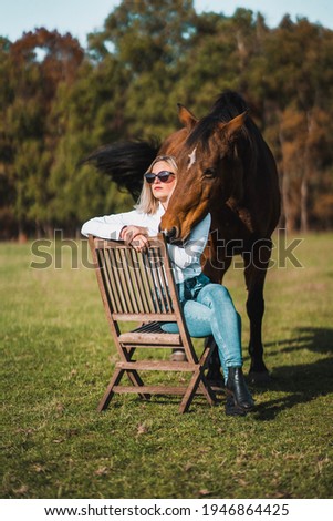Woman sitting on a chair enjoying the sun while having her horse behind her