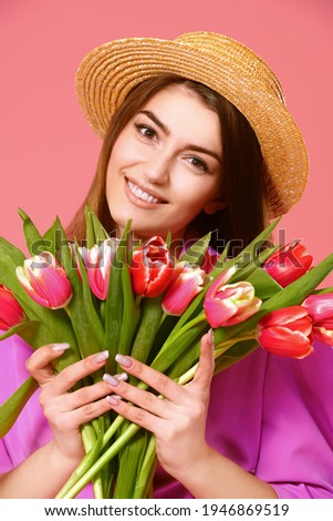 Attractive girl in a pink dress and a straw hat holds a bouquet of tulips flowers and smiles. Spring mood. Mother's Day. Valentine's Day. Pink background.