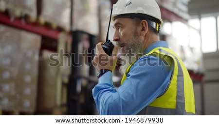 Senior warehouse manager using walkie talkie at workplace. Aged male foreman supervising work of modern factory storehouse communicating over portable radio Royalty-Free Stock Photo #1946879938