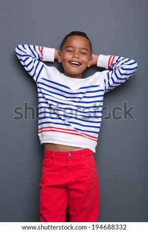 Portrait of a cute little black boy smiling with hands behind head against gray background