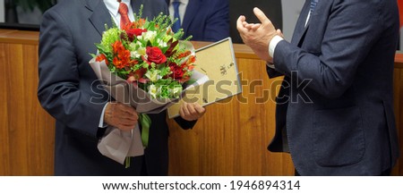 Men in business suits - officials, businessmen, teachers or lawyers - participants in the awards ceremony. Presentation of a certificate of honor and a bouquet of flowers. No face Royalty-Free Stock Photo #1946894314