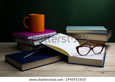 Stack of books with eye-glasses and a cup on a table. Low-key still-life photo, made on studio with black background and softbox