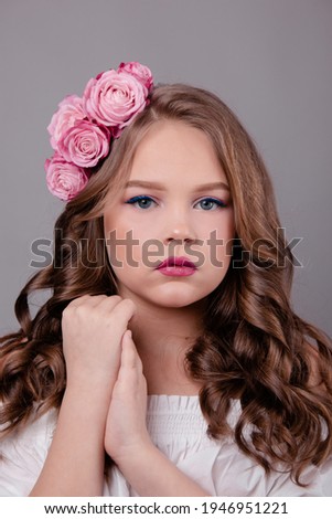 brunette teenage girl with pink roses in her hair on gray background. fashion photo. flowers in curls on the head.