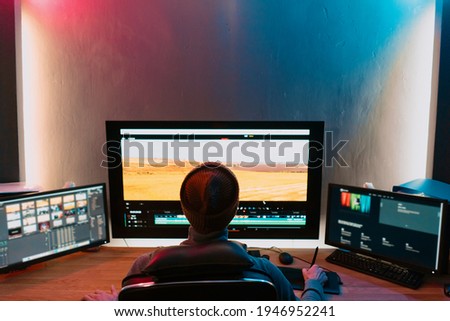 Attractive Male Video Editor Works with Footage or Video on His Personal Computer, he Works in Creative Office Studio or home. Neon lights Royalty-Free Stock Photo #1946952241