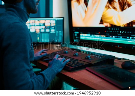 Attractive Male Video Editor Works with Footage or Video on His Personal Computer, he Works in Creative Office Studio or home. Neon lights Royalty-Free Stock Photo #1946952910