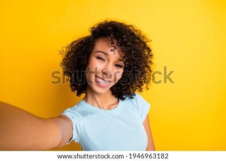 Photo of funny charming dark skin curly girl dressed blue t-shirt making selfie isolated yellow color background