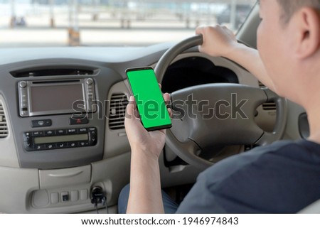Mock up of man using mobile smart phone inside a car. Driver hand holding blank green screen smartphone, searching address and pin location via map navigator application, transportation technology 