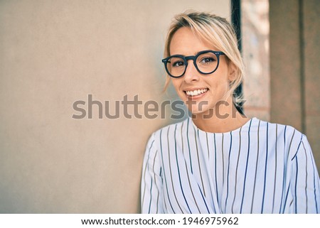 Young blonde businesswoman smiling happy leaning on the wall at the city.