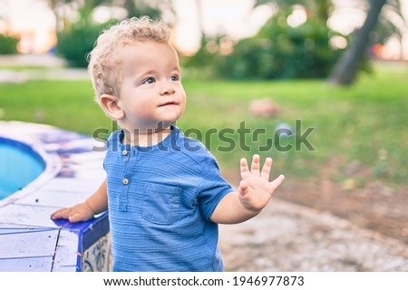 Cute and happy little boy having fun at the park on a sunny day. Beautiful blonde hair male toddler playing outdoors