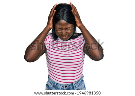 African young woman wearing casual striped t shirt suffering from headache desperate and stressed because pain and migraine. hands on head. 