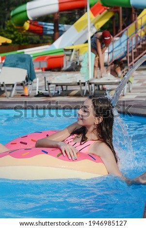Beautiful young girl on an inflatable ring. Smiling happy girl swims on an inflatable matt circle in the pool against the background of water slides