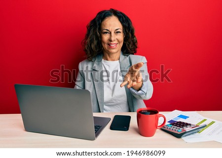 Beautiful middle age woman working at the office drinking a cup of coffee smiling cheerful offering palm hand giving assistance and acceptance. 