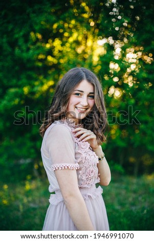 portrait of a brunette girl in a pink dress in the park. girl on a green background. beautiful summer photo