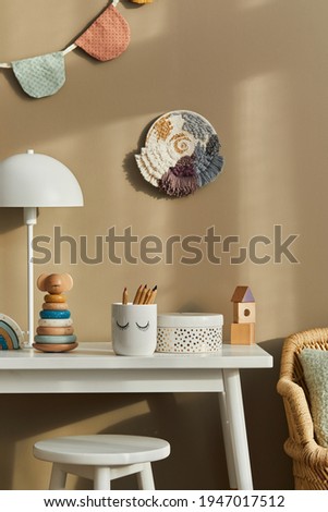 Interior design of stylish kid room space with white desk, wooden toys, child accessories, white lamp, cozy decoration and hanging cotton flags on the beige wall. Template.