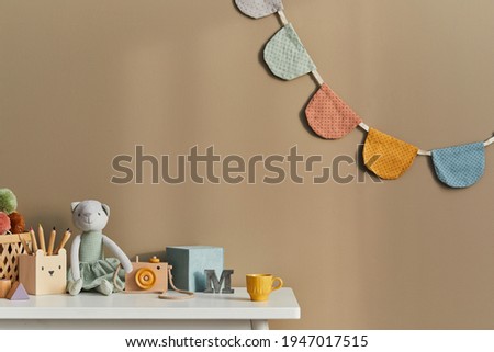Interior design of stylish kid room space with white shelf, wooden toys, child accessories, cozy decoration and hanging cotton flags on the beige wall. Template.
