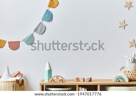 Stylish scandinavian newborn baby room with toys, plush animal, photo camera and child accessories. Cozy decoration and hanging cotton balls on the white wall. Copy space.