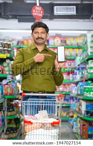 Happy man pointing at a blank screen of mobile phone at grocery store Royalty-Free Stock Photo #1947027154