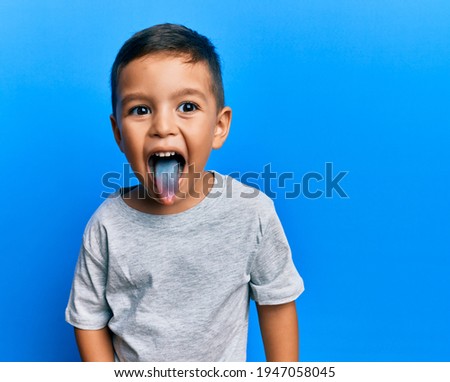 Adorable latin toddler showing blue tongue standing over isolated background.