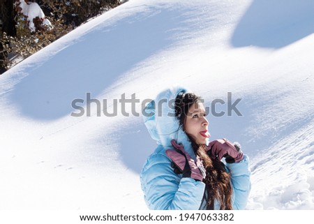 Beautiful woman wearing winter coat and sticking out tongue in snow