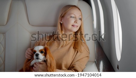 Elegant mature woman sitting inside private jet with adorable dog. Portrait of confident wealthy business lady travelling first class with cocker spaniel pet Royalty-Free Stock Photo #1947104014