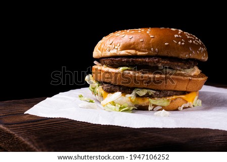 A kraftburger of two beef patties on a wooden table, isolated on a black background.