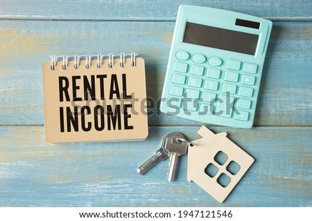 The word rental income is written in a notebook that sits on a gray desktop along with a laptop. Business image