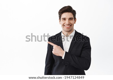 Confident realtor, businessman in suit pointing aside and smiling, showing good promo offer, best deal in real estate, standing over white background